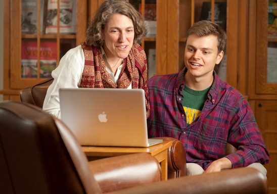 Professor and student look at an open laptop