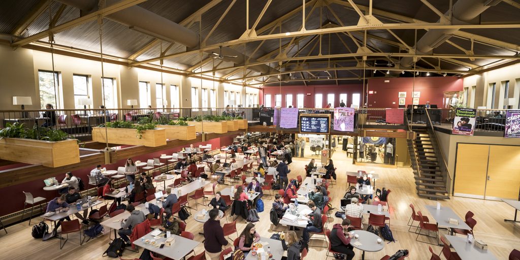 A crowd of people gather at tables for lunch in the large, vaulted space of Sayles-Hill Campus Center