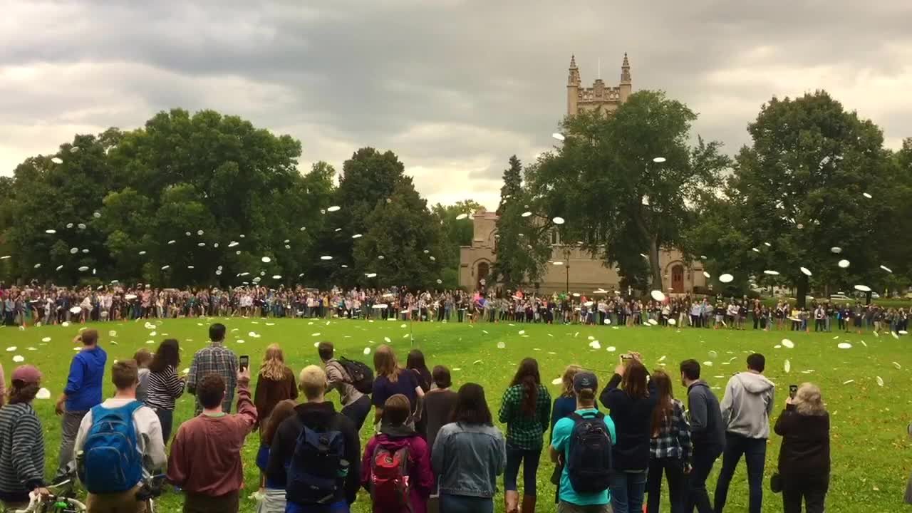 Video: A circle of several hundred students throw Frisbees on the Bald Spot
