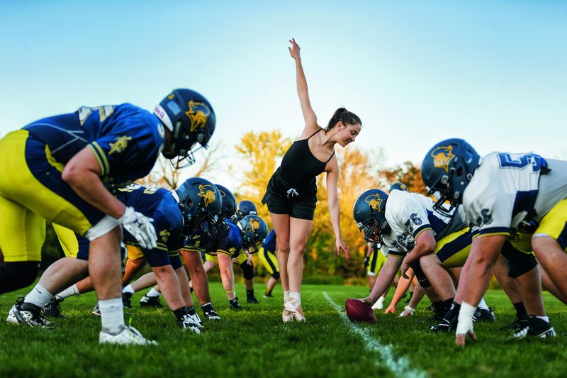A ballerina standing en pointe in the middle of a football line of scrimmage