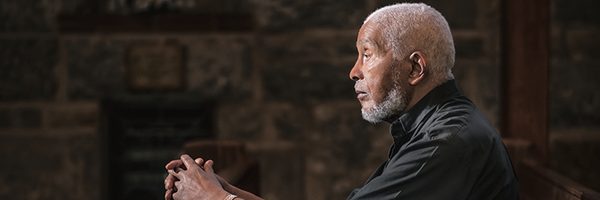 Earl Neil sits in a church pew beneath a stained glass window