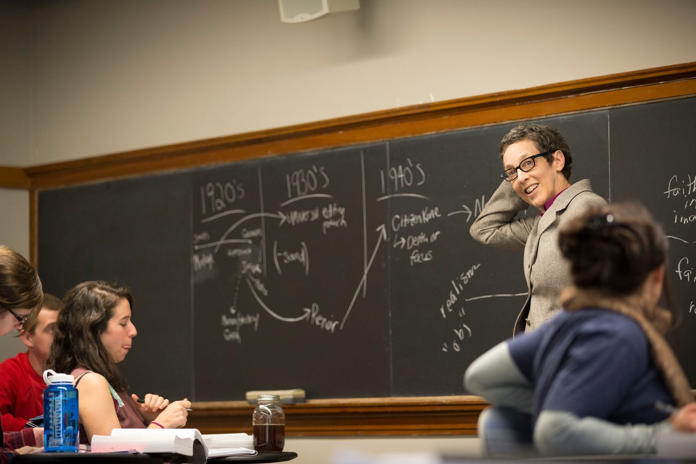 A professor stands at a blackboard in a classroom