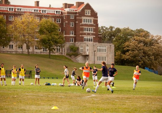 students play soccer with carleton in the background