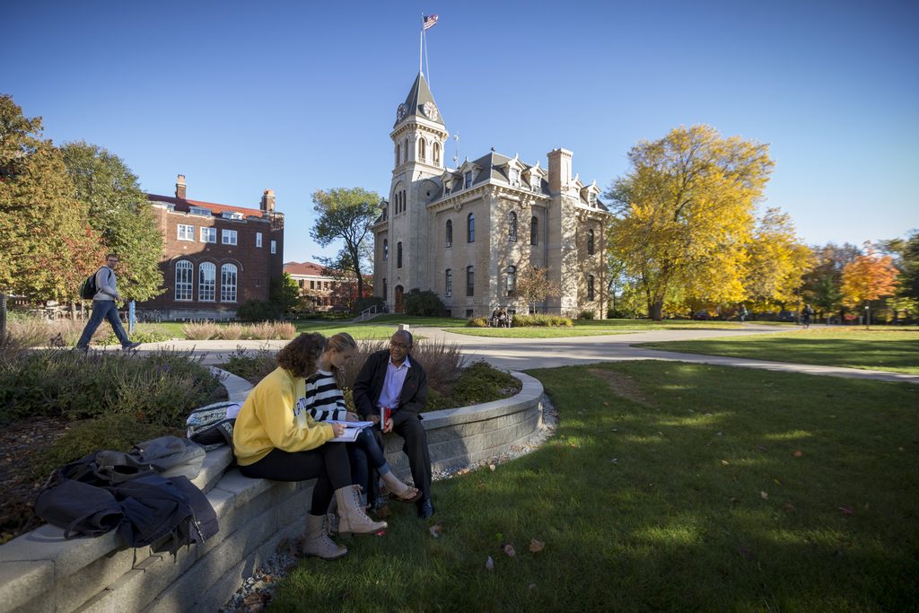 Two students sit with a professor outside a residence hall