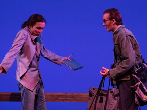 A man with a journal and pencil in his hand speaks to an older man who is carrying luggage.