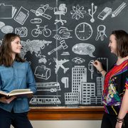 Three students stand in front of an elaborately-illustrated chalkboard