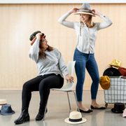 Two students pose with a basket of different hats, spilling onto the floor