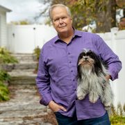 A man poses with a dog under his arm